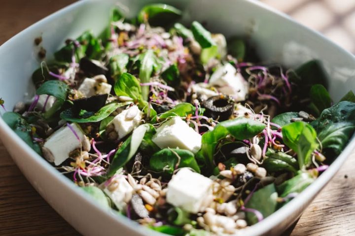 Fresh spinach salad with feta, olives, and sprouts, served in a sunlit bowl.
